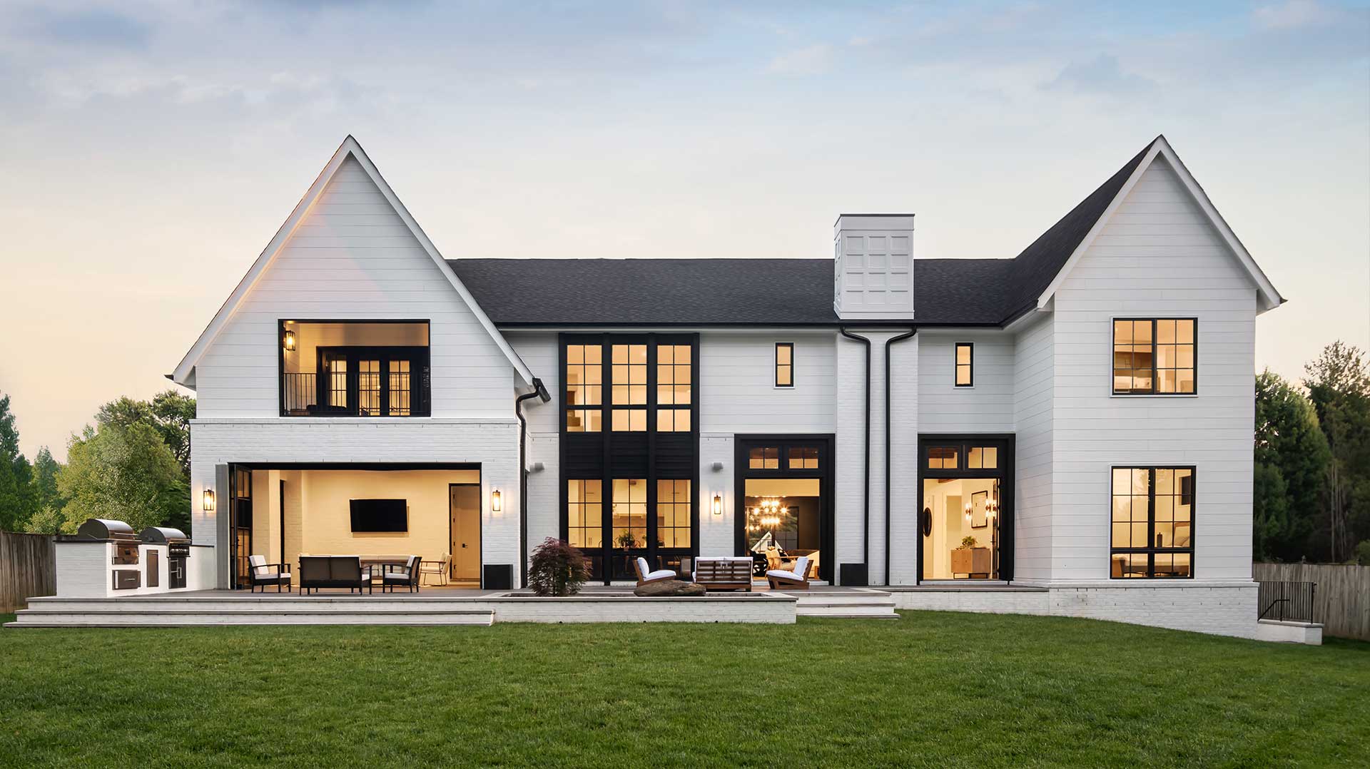 A completed Coastline home at dusk, its interiors lit and open to the lawn